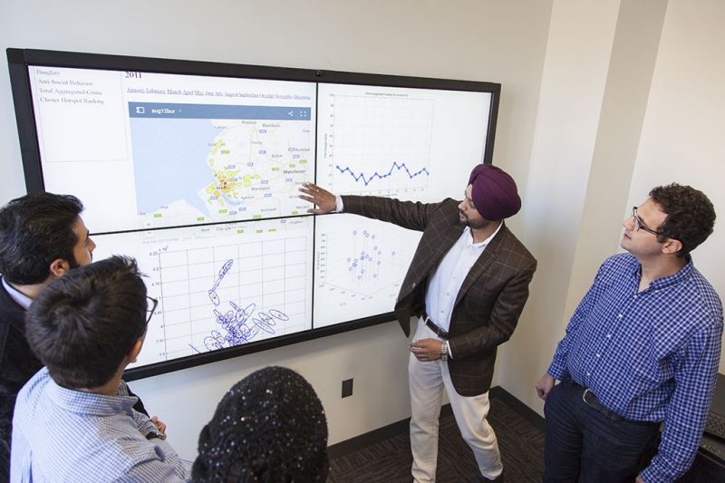 In the photo, researchers examine and discuss a smart board covered with data.