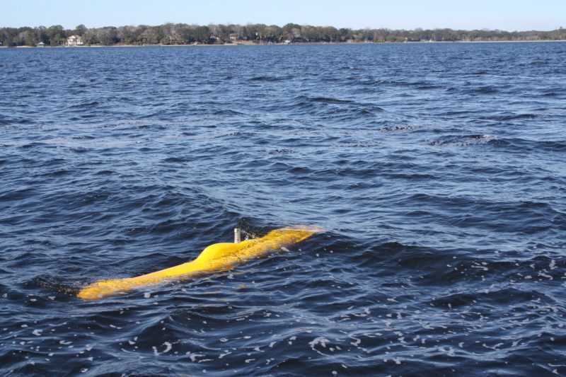 Photo of a small, orange autonomous underwater vehicle partially submerged in blue water.