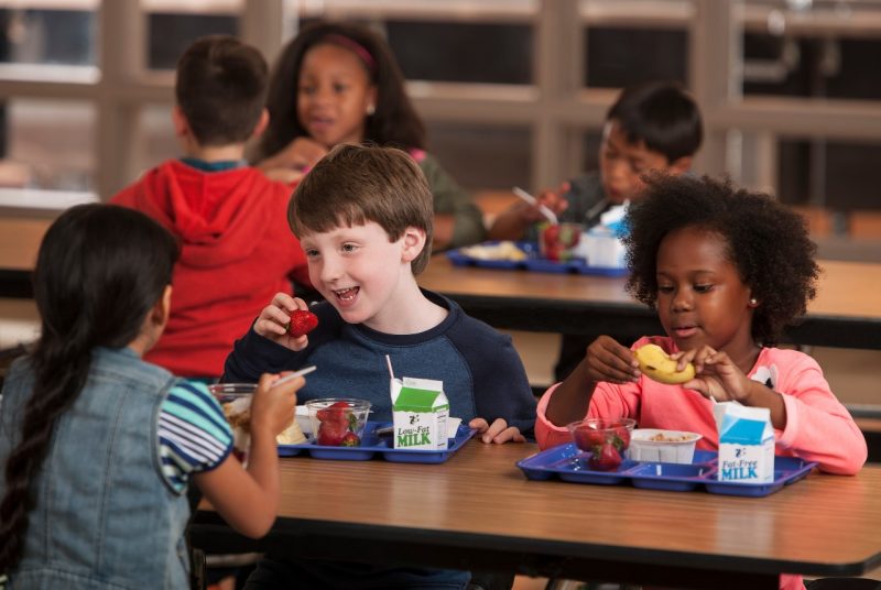 Six elementary students eat breakfast in a school cafeteria.