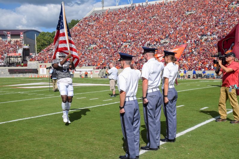 flag cadets Three cadets stand at attention as a Hokie football player jogs toward them carrying the American flag.