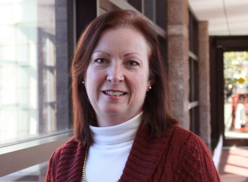 Image of Karen Herrington smiling, standing in a windowed hallway.