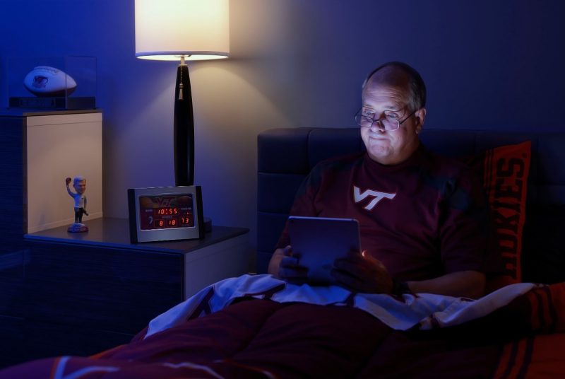 An employee checks email while his bedside clock shows the time of 10:55 p.m..