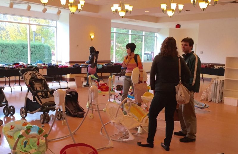 Four graduate students, three of whom are carrying bags, examine children's equipment and clothes at a recent Little Hokie™ Hand-Me-Down event at the Graduate Life Center's multipurpose room.