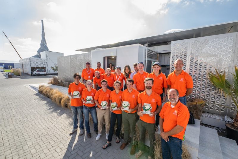 A team of students and faculty wearing orange polo shirts stands in front of their award-winning house.