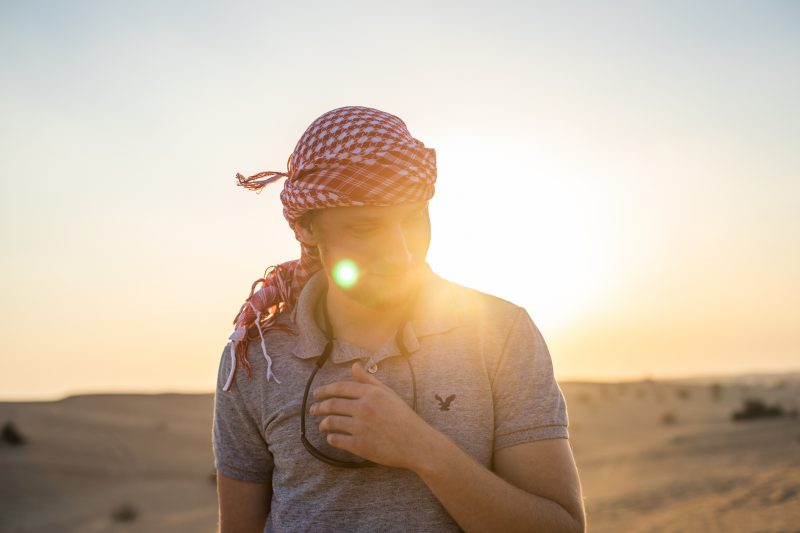 Man stands in desert wearing a red and white checkered head scarf.
