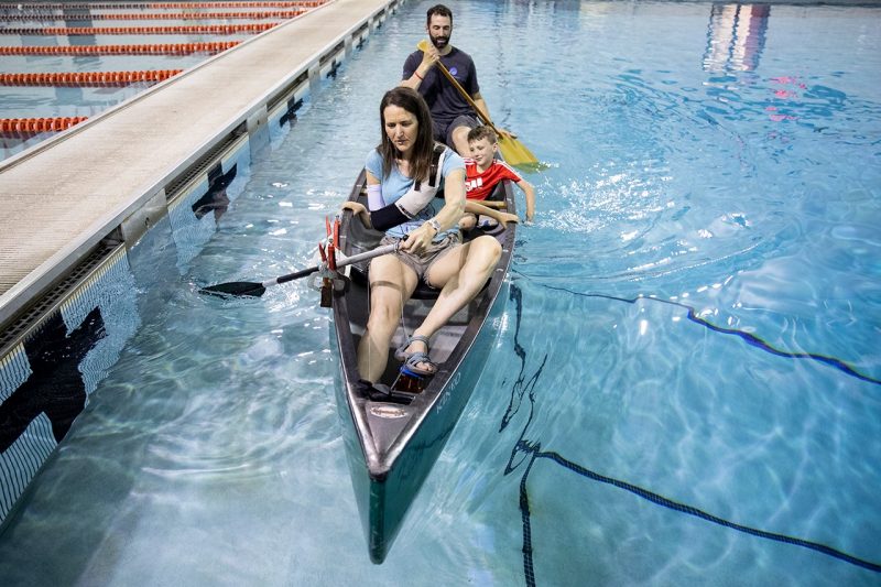 With one arm, a woman and her family paddle a canoe around the pool at War Memorial Hall