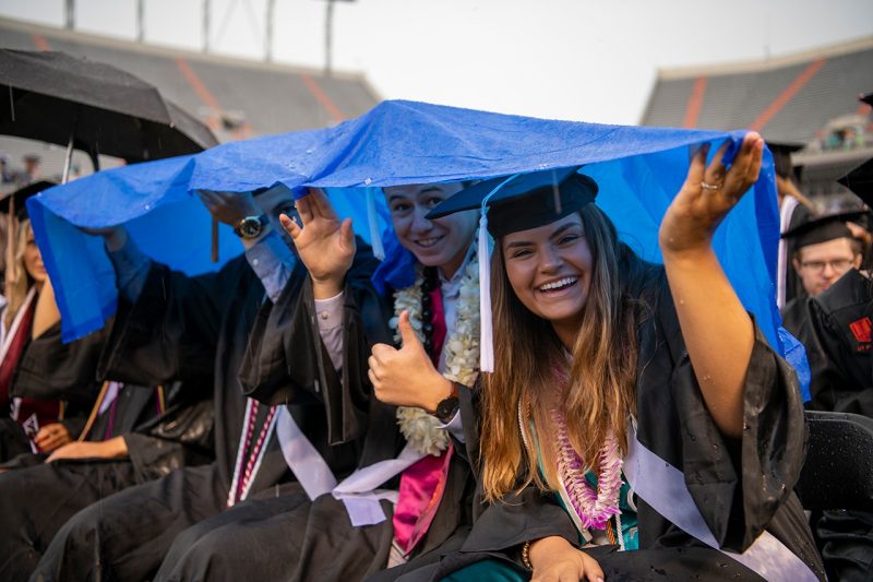 Graduates keep dry beneath a tarp