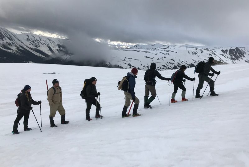Seven students in a row hike up a snow-covered slope.