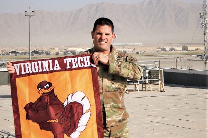 U.S. Army Col. Barry “Chip” Daniels holds a Virginia Tech flag while deployed to Afghanistan.