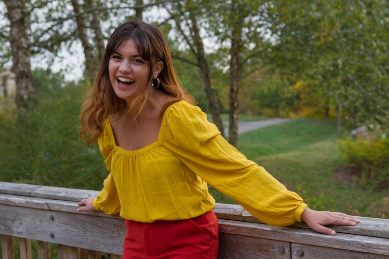 Portrait of a smiling Ellie Muraca wearing a yellow top and red pants 