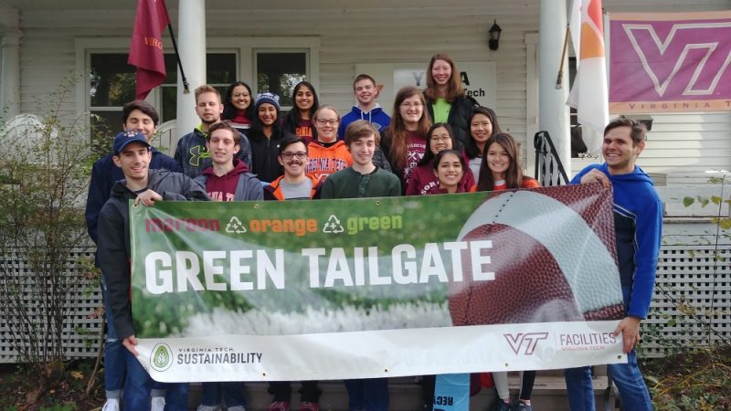 Green tailgate team poses for a photo, holding a sign that says maroon, orange, green, Green Tailgate