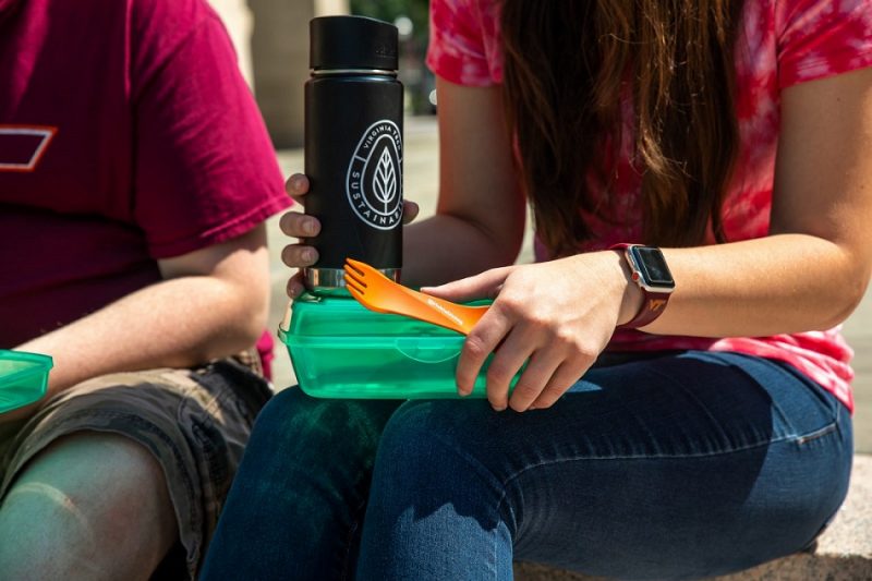 A student holds a clear, green sustainable to-go container
