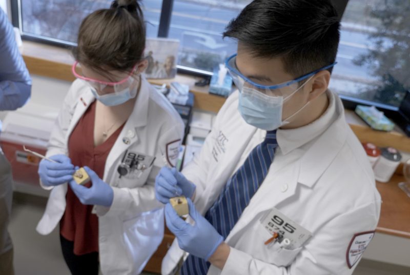 Female and male medical students wearing white coats and masks practicing dental techniques