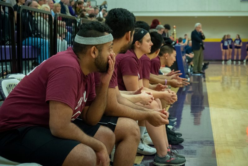 Players watch a basketball game from the sidelines.