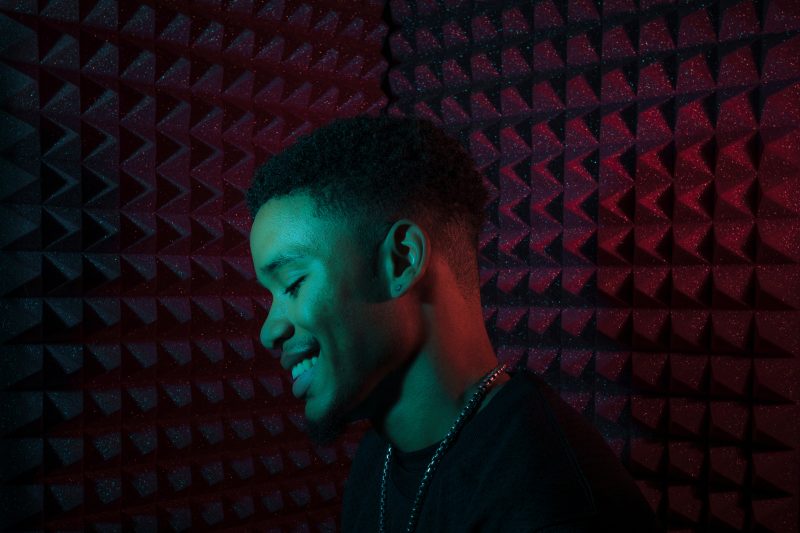 Profile picture of DeRay Manning inside recording studio, with blue and red lighting. 