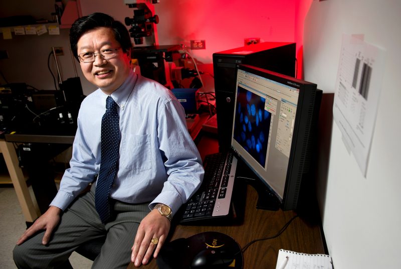 Portrait of XJ Meng in a lab next to computer