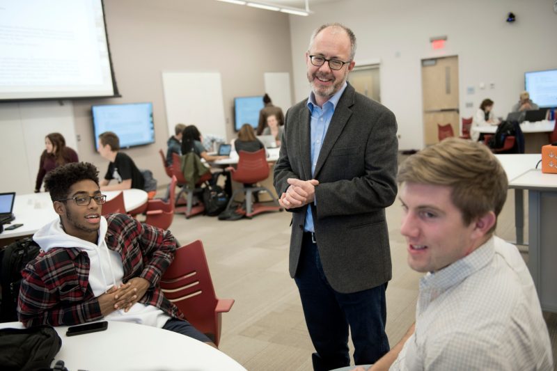 Mark Embree, professor of mathematics, talks with students in his Computational Modeling and Data Analytics capstone project class in this November 2017 photo. Embree is wearing a dress shirt and sports coat as he stands near the students.