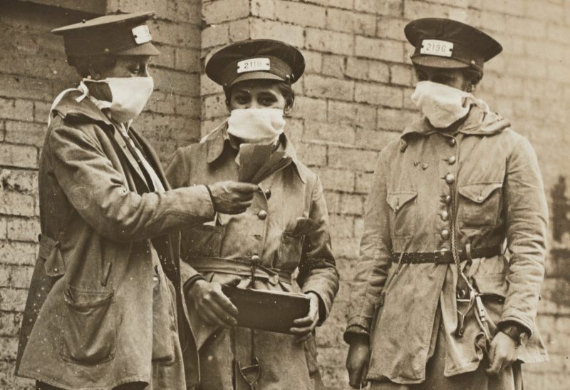 Women conductors in 1918 New York stand nearby on a city street and wear face masks to prevent the spread of influenza during the 1918 flu pandemic. National Archives
