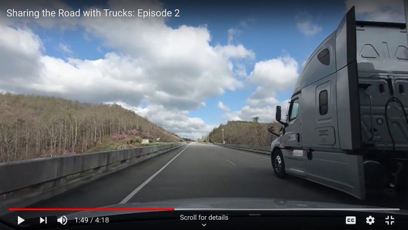 A large truck drives in the righthand lane of a two-lane road across a bridge. The truck is approaching a group of trees on either side of the street. This image was included as part of the Sharing the Road video series and is meant to demonstrate the dangers of lingering in a truck's "no zone".