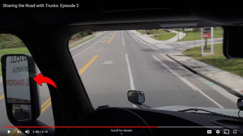 A truck prepares to make a turn on a road. There is an arrow pointing to the truck's lefthand side mirror.