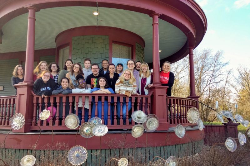 A group of students and faculty stand on the porch of a historic house.