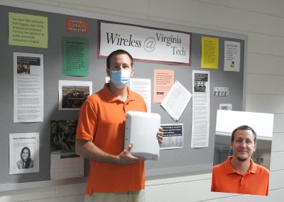 Person wearing protective face covering stands in front of Wireless Communications notice board holding radio test equipment