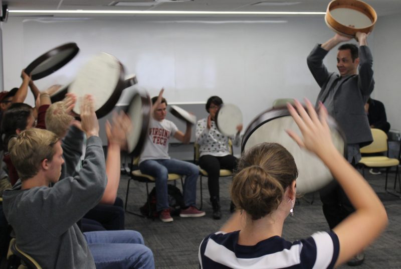 Artist Karim Nagi and a group of Virginia Tech students hold their drums over their heads during a workshop.