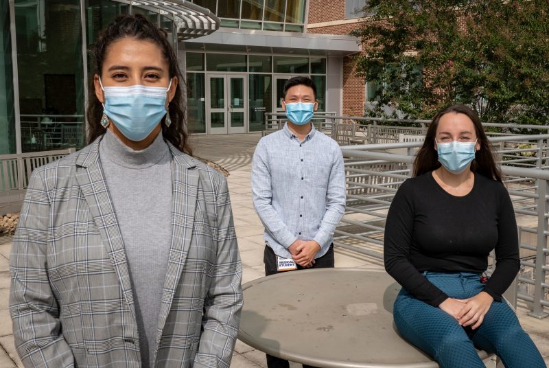 Three students wearing masks gathered on an outdoor patio.