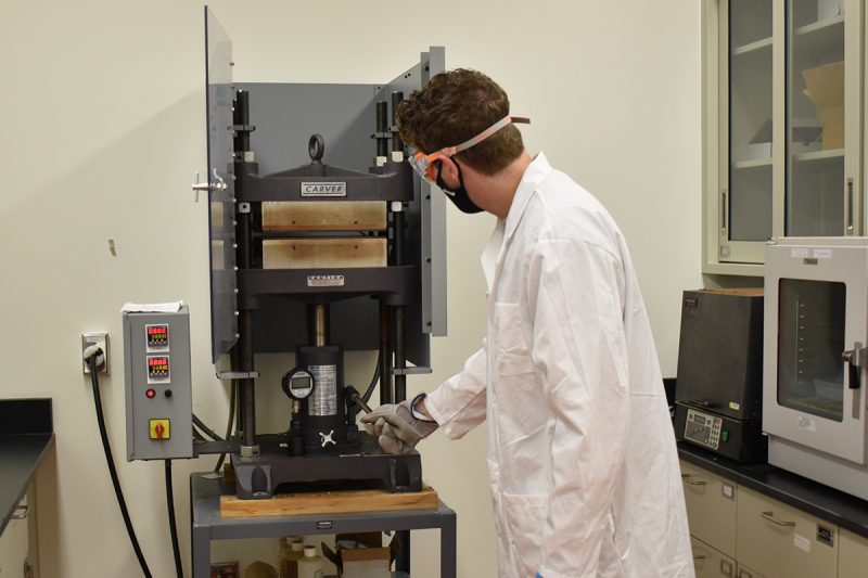 student using a mechanical press in the Materials Characterization Lab 