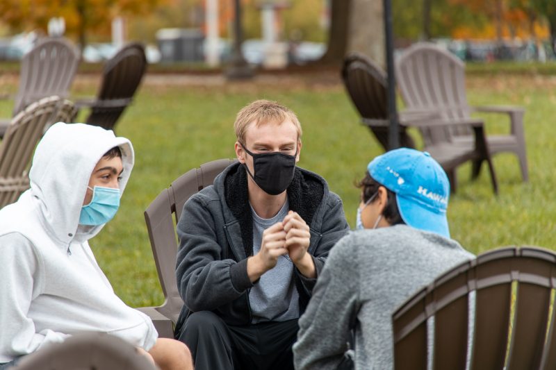 Three members of a Living-Learning Program chat outside while wearing face masks.