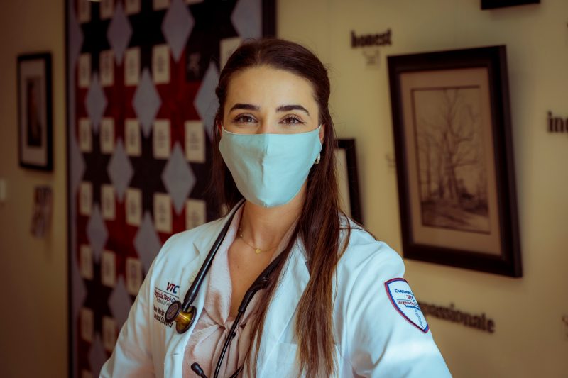 Female medical student with white coat and stethescope stands in front of a colorful wall.
