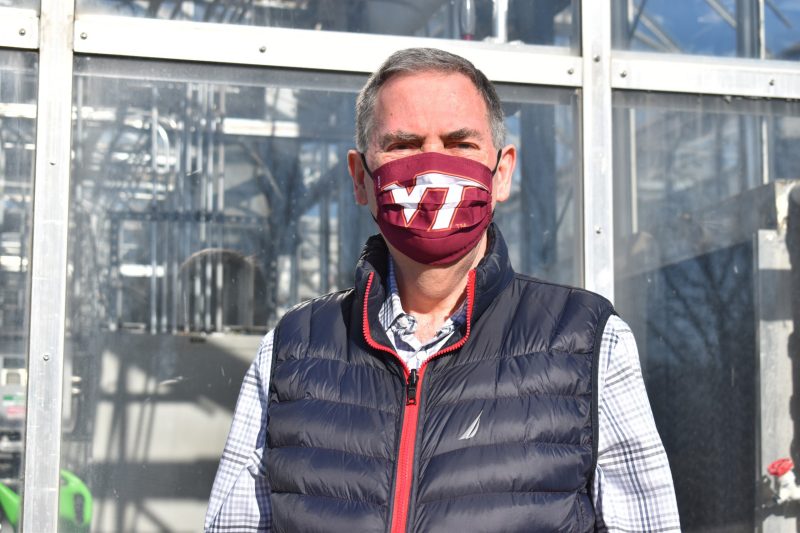 Erik Nilsen poses at the Virginia Tech Plant Growth Facility built on Smithfield Road. He founded the facility in 2007. Nilsen is wearing a Virginia Tech branded face mask and a plaid shirt. Photo by Steven Mackay.