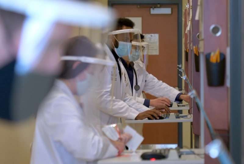 Students wear face masks and shields waiting to enter a standardized patient exam room