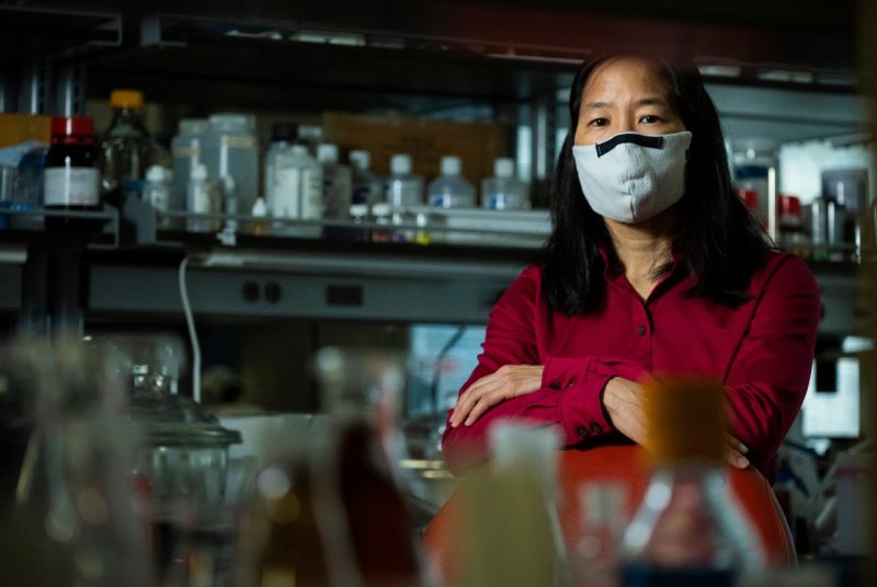 Woman wearing red shirt and mask sitting in scientific laboratory