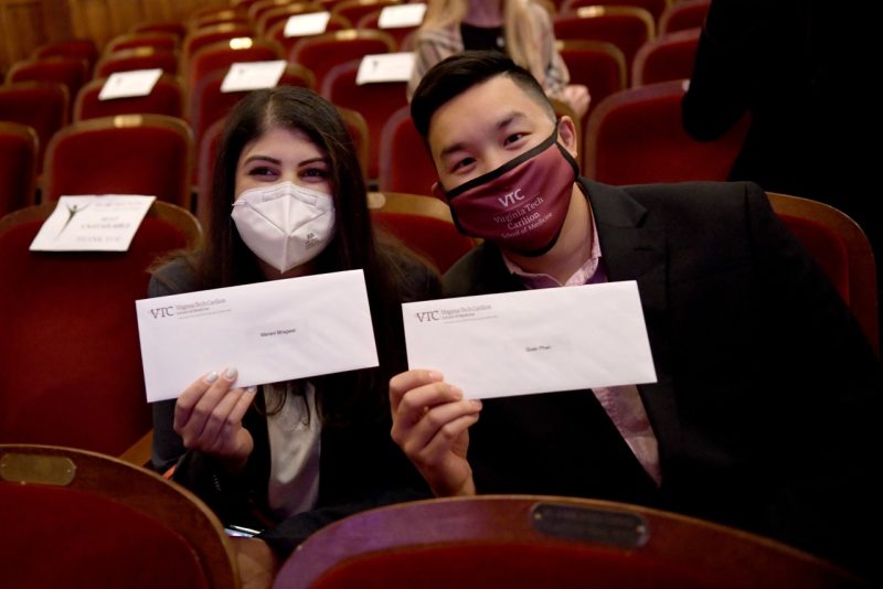 A student couple holds up their Match Day envelopes
