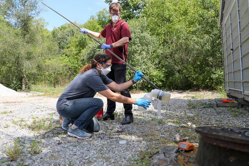 Two people collect a sample of wastewater