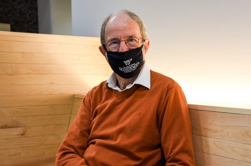 Kenneth Eriksson, wearing mask with the Department of Geosciences logo, poses for a photograph whilst sitting down.