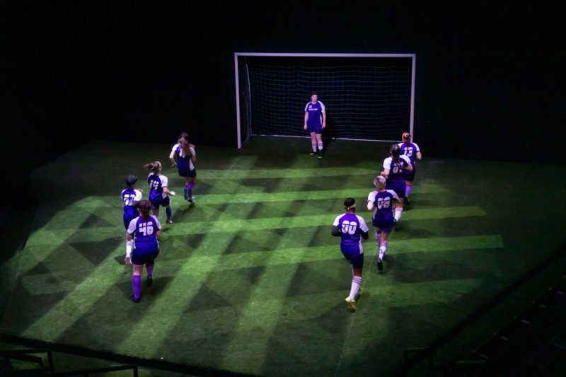 "The Wolves" Lighting Design Theatre set featuring soccer players in blue uniforms at the goal line. Green netting is reflected on the ground.
