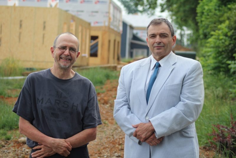 Two men standing side by side in front of a house under construction.