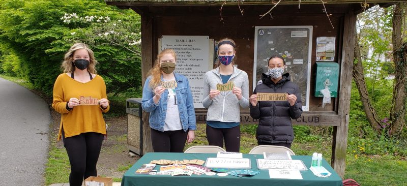 Four young people wearing masks stand at a table outside. They hold signs that say: Reduce, Reuse, Recycle, #VTEarthWeek