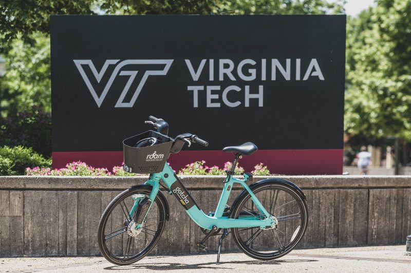 Teal e-bike parked in front of Virginia Tech entrance sign by Squires Hall.