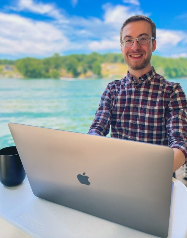 Glenn Feit sitting in front of a laptop with a lake behind him