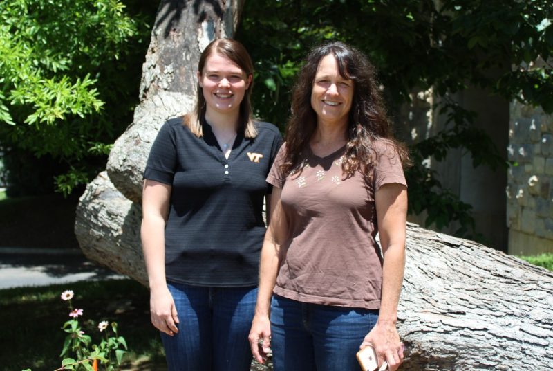Two women stand side by side in front of a large tree