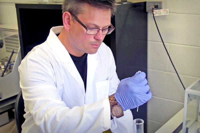 Brandon Jutras, assistant professor of biochemistry in the Virginia Tech College of Agriculture and Life Sciences and the recipient of the 2021 Emerging Leader Award, pipetting into a flask in the lab. He is wearing glasses, a white lab coat, and periwinkle gloves.