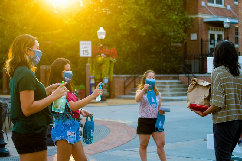 Three students wearing masks handing out masks and hand sanitizer 