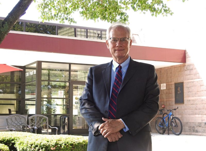 Scott Midkiff wearing suit and tie standing in front of building with glass atrium