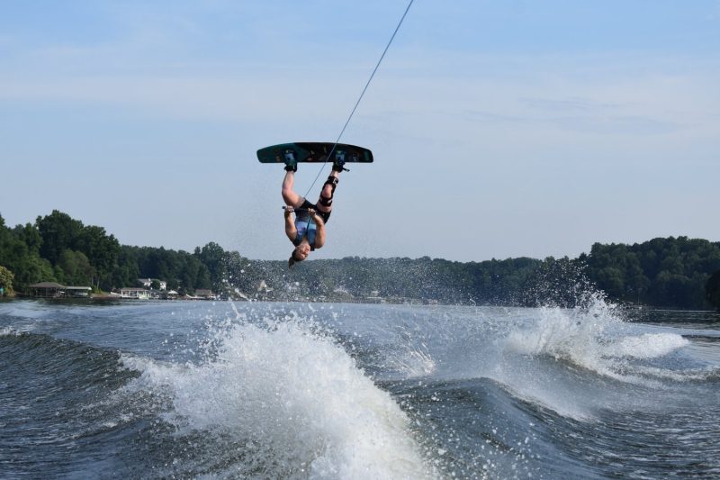 Joy Manning upside down in the air on a wakeboard above a boat's wake on a lake