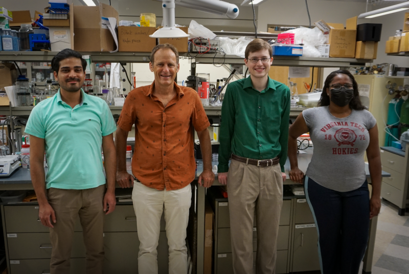 Four people smile toward the camera, standing in front of a laboratory bench. 