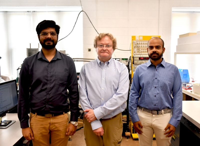 Left to right, Adbhut Gupta, Jean Heremans, and Gitansh Kataria in their lab at Robeson Hall. The three men, each wearing a dress shirt, stand in front of various lab machines.