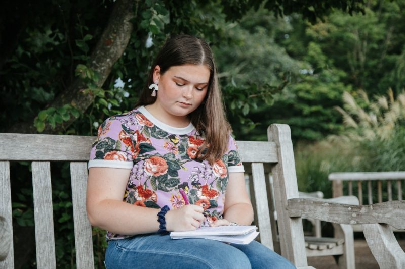Person sitting on bench and writing in a journal